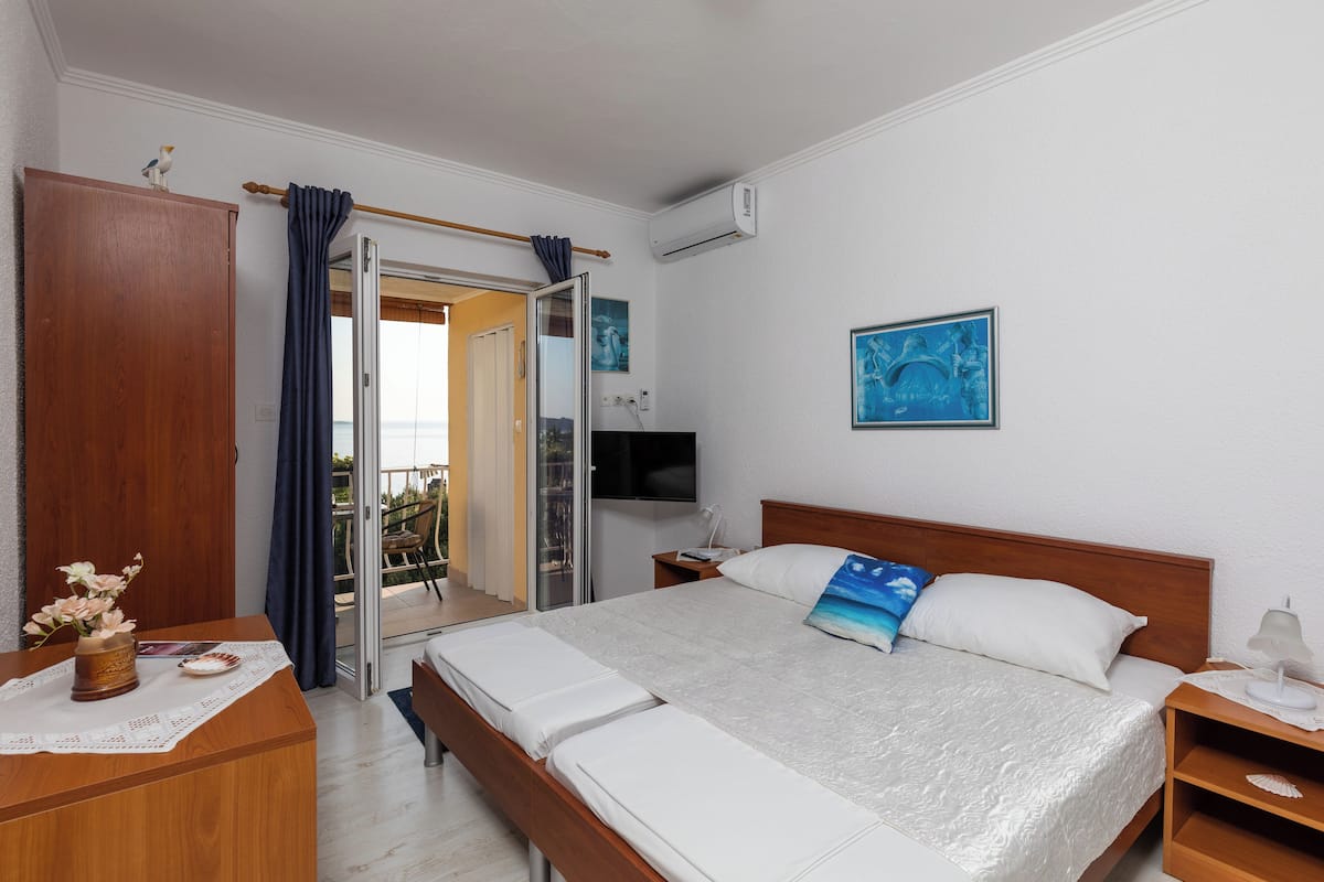 A hotel room with a bed, a wooden nightstand, a TV, and a view of the outdoors.