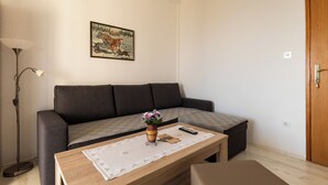 A living room with a sofa, a coffee table with a vase and remote control, a floor lamp, and a door. - Apartments Belenum (Zupa dubrovacka)