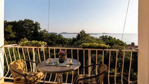 A balcony with a round table, two wicker chairs, and a view of the sea. - Apartments Belenum (Zupa dubrovacka)