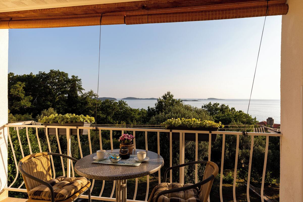 A balcony with a round table, two wicker chairs, and a view of the sea.