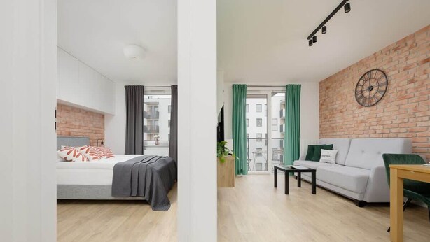 Un apartamento moderno con una cama, un sofá, una mesa de comedor y una pared de ladrillo.
