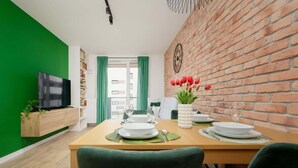 Un comedor con pared de ladrillo, una mesa de madera dispuesta para cuatro personas y un televisor sobre un mueble de madera.