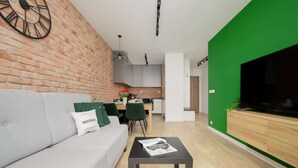 Una sala de estar moderna con una pared de ladrillo, un sofá gris, una zona de comedor con una mesa y sillas, y una pared de acento verde.