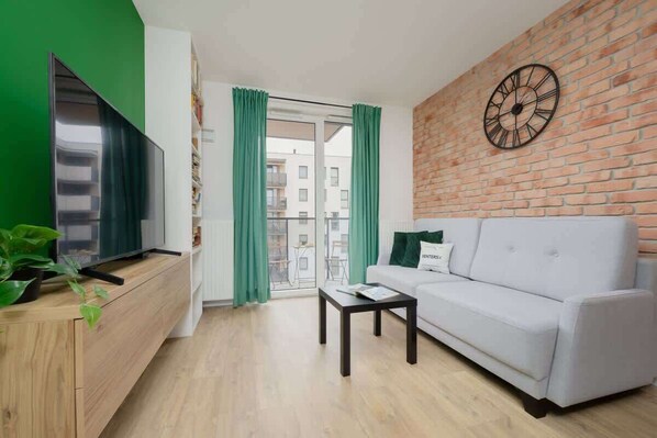 Una sala moderna con una televisión de pantalla plana, un sofá blanco, una mesa de centro de madera y una pared de ladrillo con un reloj.