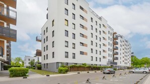 Un edificio residencial moderno de varios pisos con balcones, una zona de estacionamiento y cielo despejado.