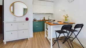 Una cocina compacta con armarios blancos, una mesa de comedor de madera y sillas negras.
