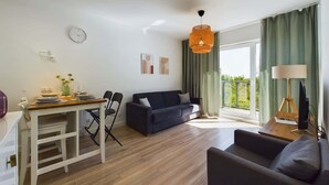 Una sala de estar moderna con suelo de madera, un sofá oscuro, una mesa de comedor con sillas y un ventanal con cortinas.
