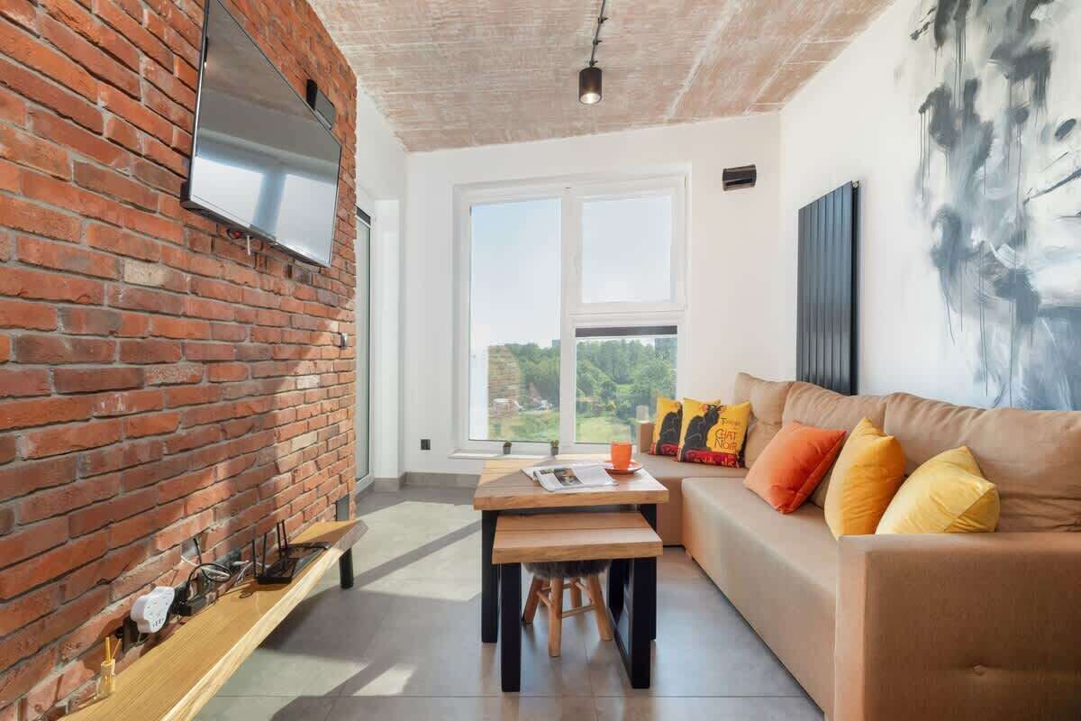 A modern living room with a brick wall, a wooden bench, a sofa with colorful cushions, and a large abstract painting.