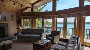 Amplia sala de estar con un ventanal que da a un lago, amoblada con un sofá, un sillón y un cofre de madera.