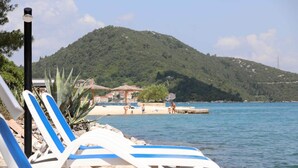 A beachside view with lounge chairs, a mountain in the background, and a clear sky. - Apartments More & Ja (Ston)