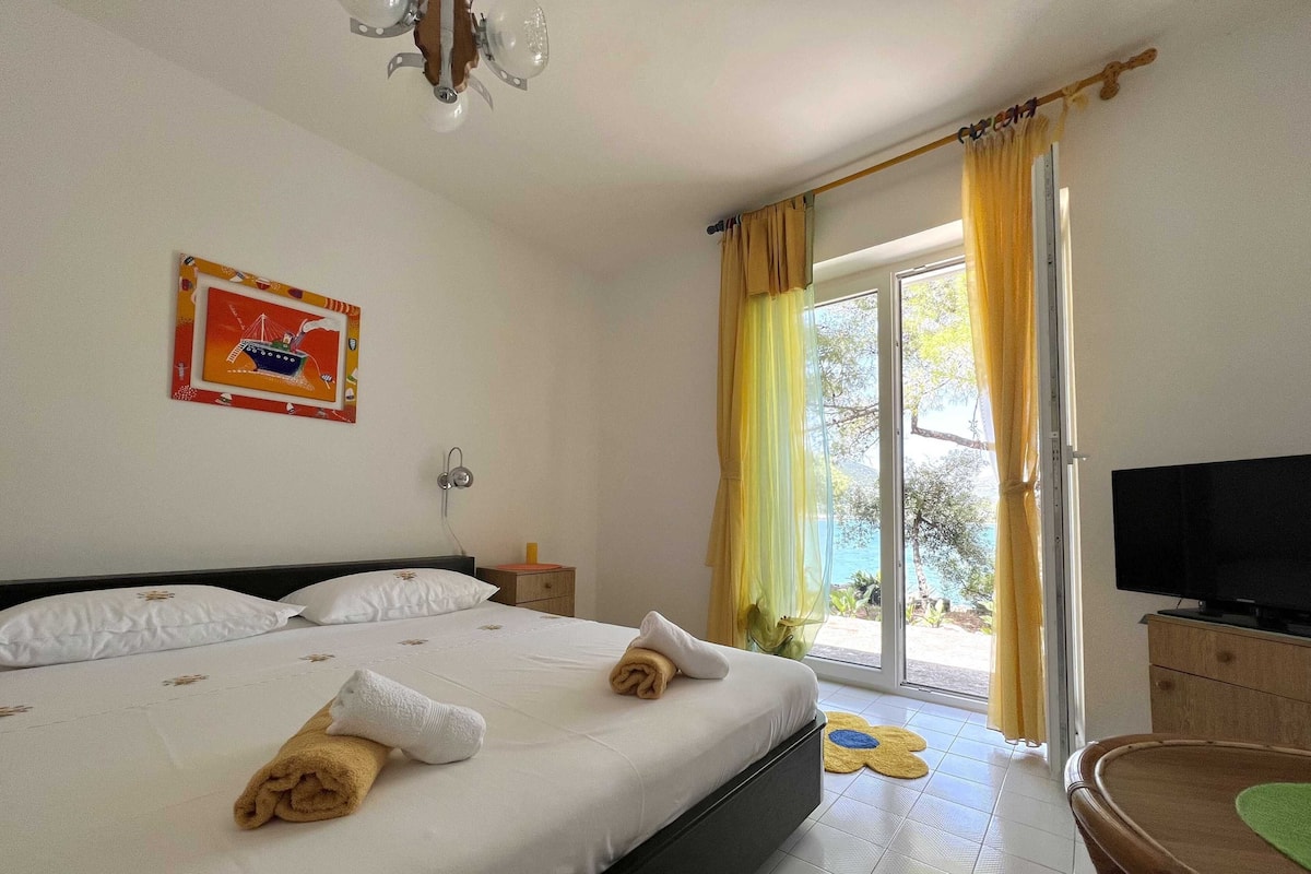 A hotel room with a bed, a television, a window with curtains, and a painting on the wall.