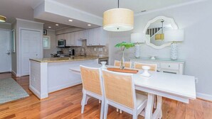 Une cuisine moderne avec des meubles blancs, un îlot central et un coin repas comprenant des chaises et une table, le tout dans des tons blancs.