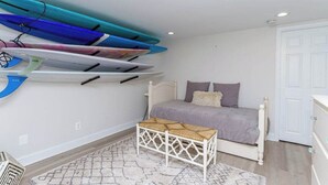 Une chambre avec un lit, un petit banc blanc et des planches de surf accrochées au mur.