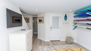 Une pièce avec une commode blanche, un téléviseur, une porte et des planches de surf accrochées au mur.