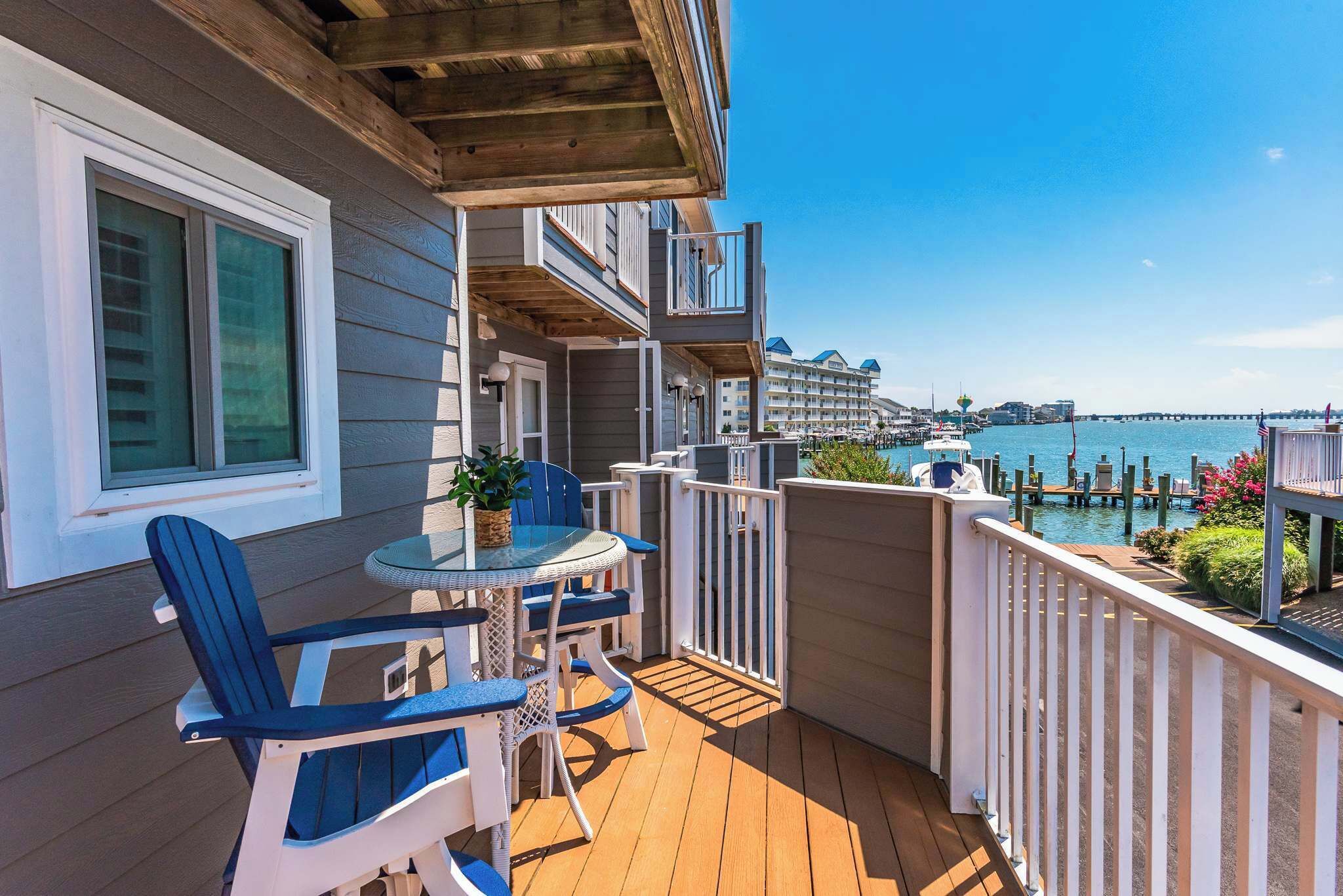 A balcony with a table and chairs, overlooking a marina with boats and a pier.