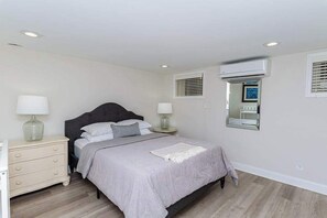 A bedroom with a bed, bedside tables, lamps, an air conditioning unit, and a window with blinds.