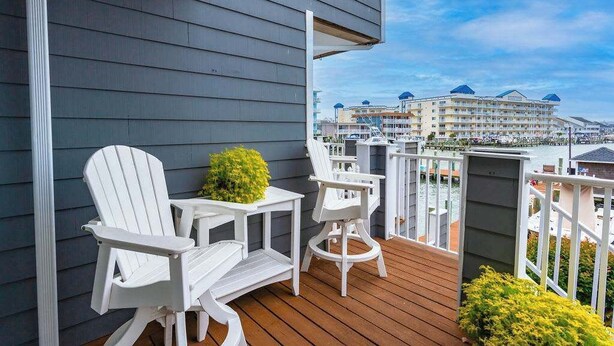 Un balcon agrémenté de chaises Adirondack blanches et d’une petite table, d’où l’on peut admirer une marina avec des bateaux, et un hôtel en arrière-plan.