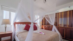Een opgemaakt bed met hemelbed, houten hoofdbord en kussens.