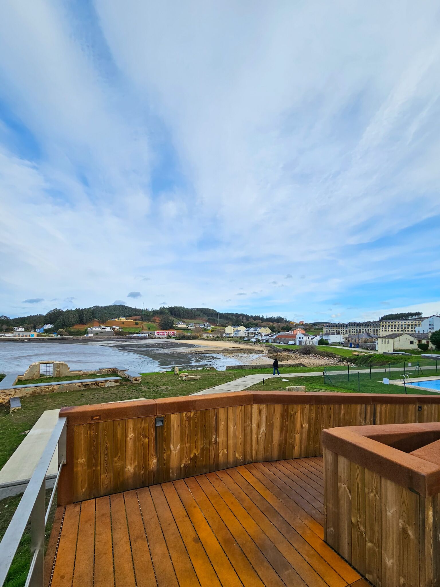 A wooden deck with a view of a beach and buildings in the distance.