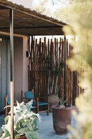 Un espacio de estar techado al aire libre con un cerramiento de bambú, una planta grande en maceta y una silla.