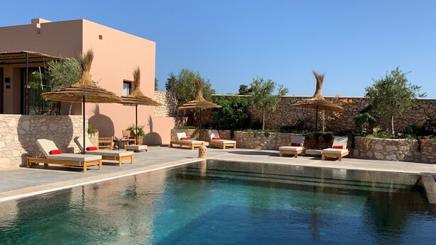 A pool area with lounge chairs and umbrellas, surrounded by stone walls and vegetation. - Dar Almajula (Essaouira)