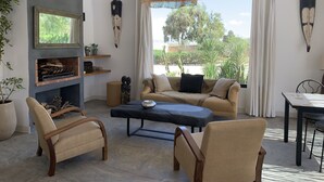 A modern living room with a sofa, two armchairs, a coffee table, a fireplace, and a large window with curtains. - Dar Almajula (Essaouira)