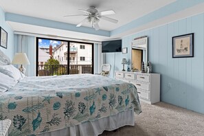 Une chambre à coucher comprenant un lit, un ventilateur de plafond, une commode, un téléviseur et un balcon avec vue sur les bâtiments.