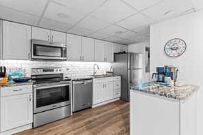 A modern kitchen with stainless steel appliances, white cabinetry, and a marble countertop.