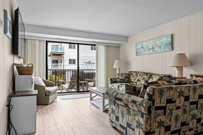 A living room with a sofa, a television, a small table, and a window with a view of a building.