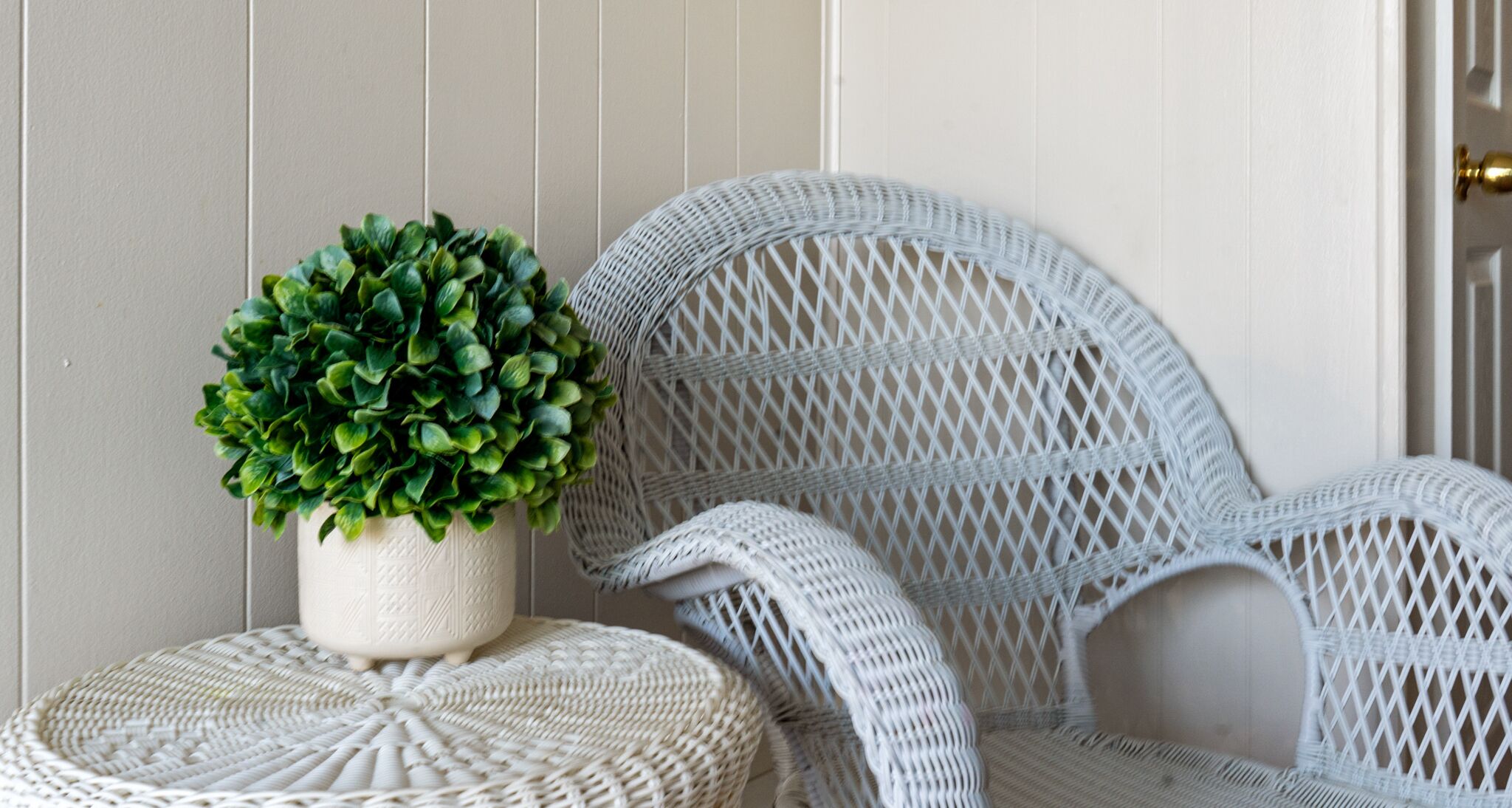 A wicker chair with a round ottoman and a potted plant beside it.