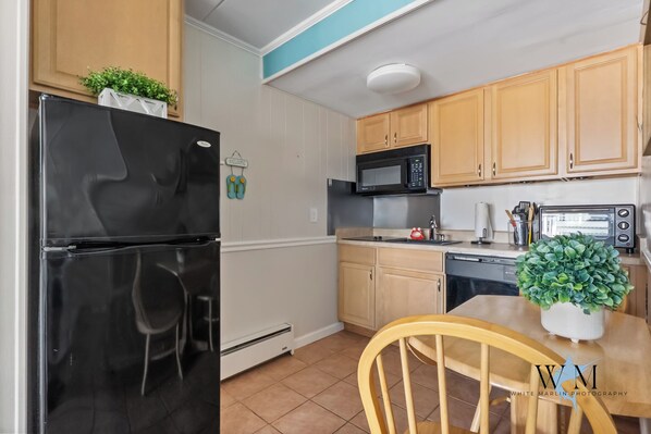 Una cocina con armarios de madera, un refrigerador negro, un microondas y un tostador. Hay una planta en la encimera y una silla en la mesa.