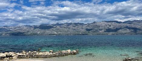 A clear view of a lake with a rocky shoreline and mountains in the background.