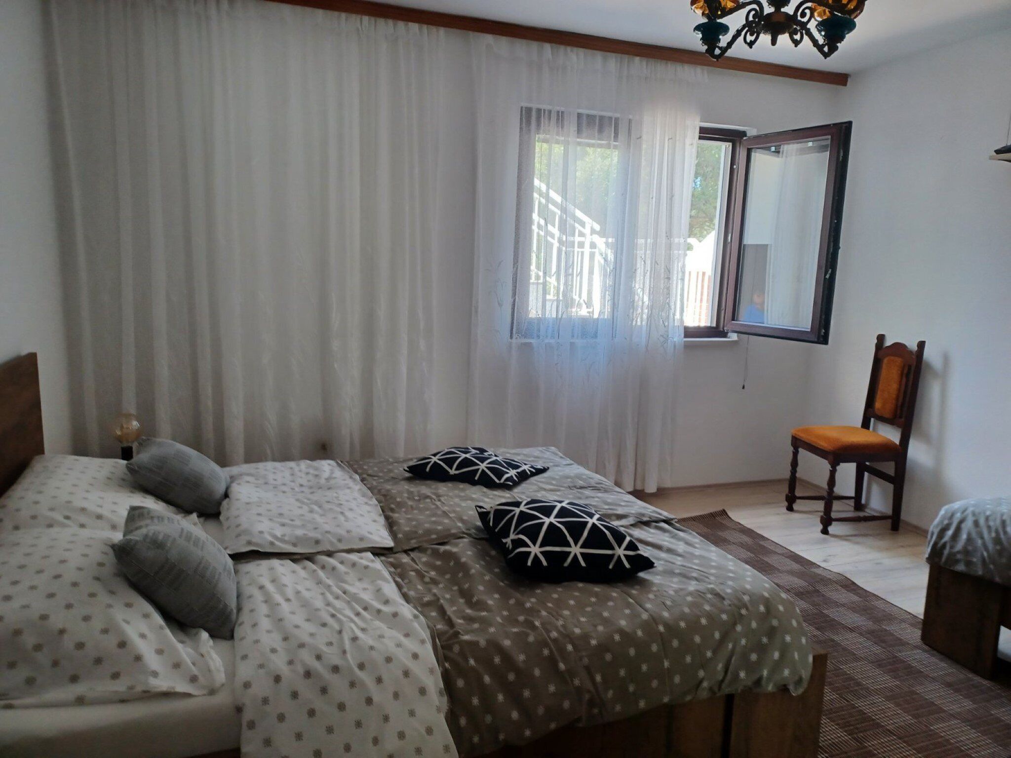 Um quarto com cama, poltrona, janela e lustre.