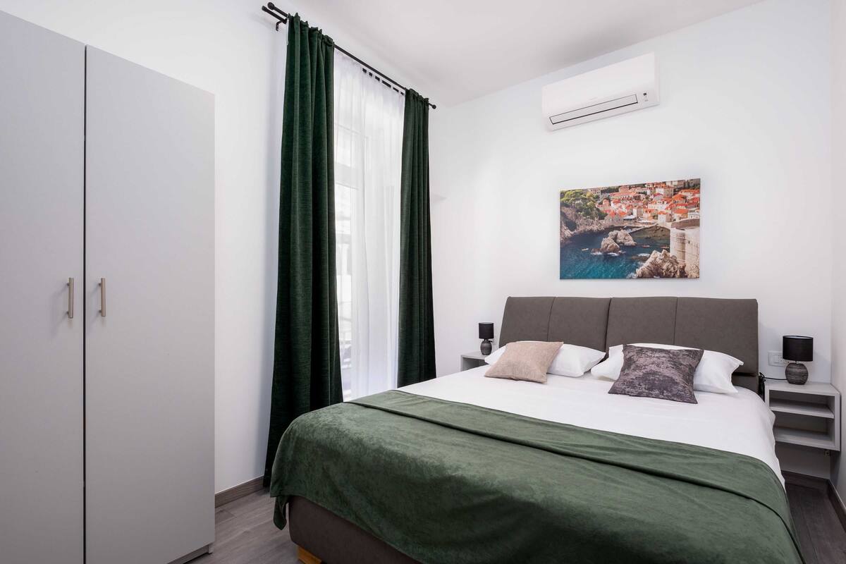 Een slaapkamer met een bed, een kledingkast, een nachtkastje, een lamp en een schilderij aan de muur.