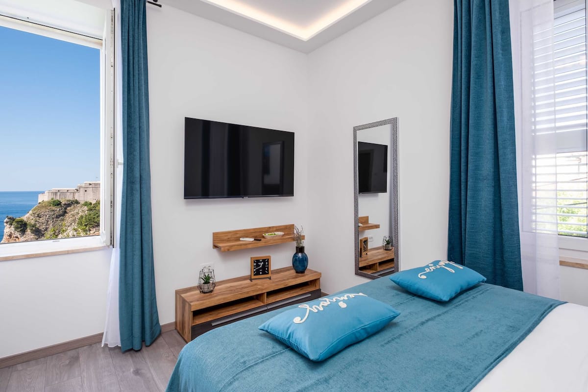 Een slaapkamer met een groot bed, een televisie, een houten console en uitzicht op zee.