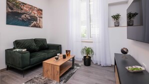 En moderne stue med en grøn sofa, et træbord, en potteplante og et fladskærms-tv på et sort stativ.