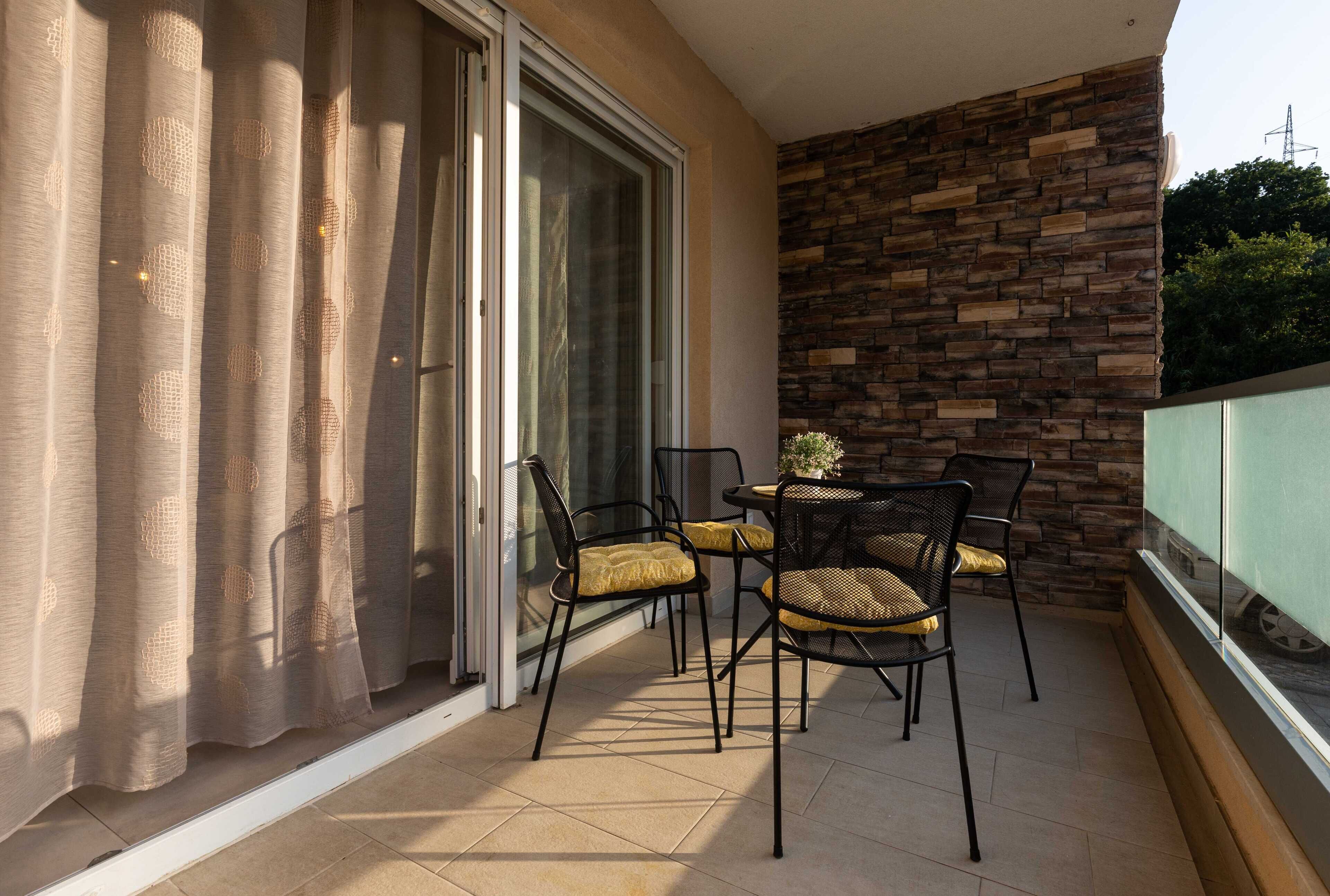 Een balkon met een schuifdeur, een stenen muur en een tafel met stoelen.