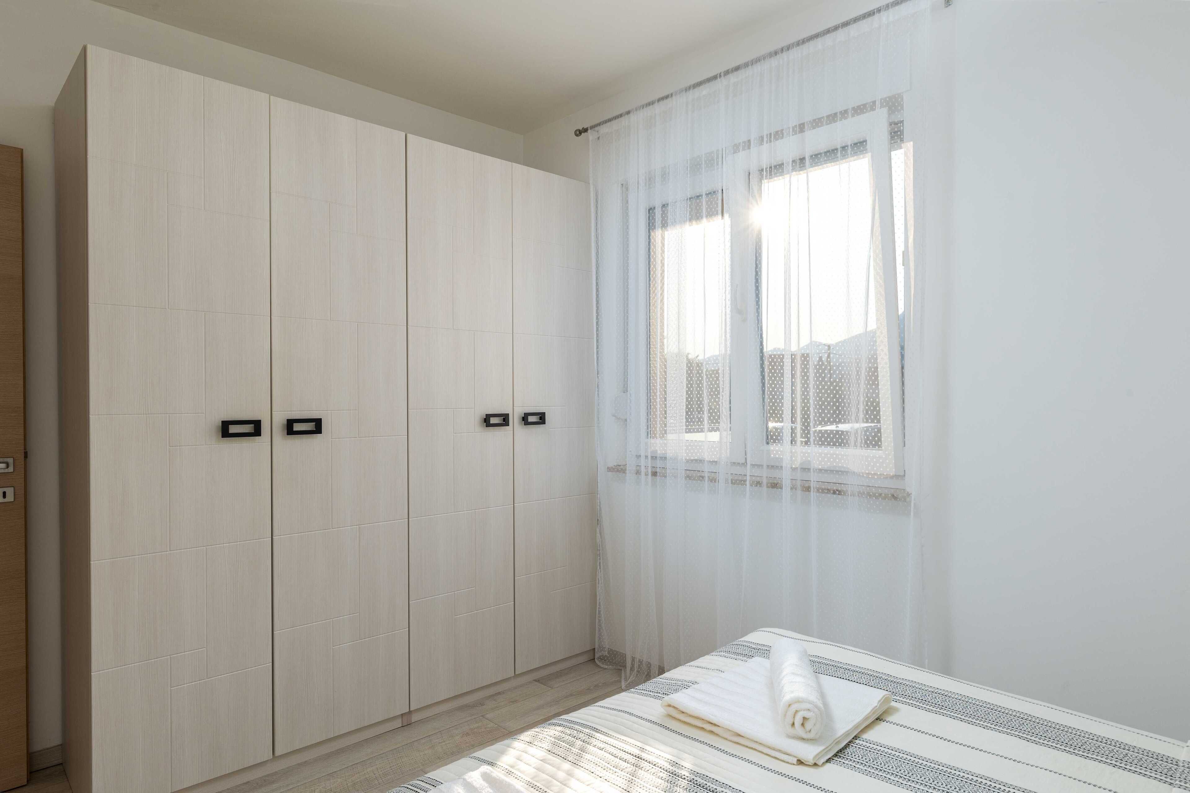 Une chambre à coucher avec un lit, une armoire et une fenêtre ornée de rideaux légers.