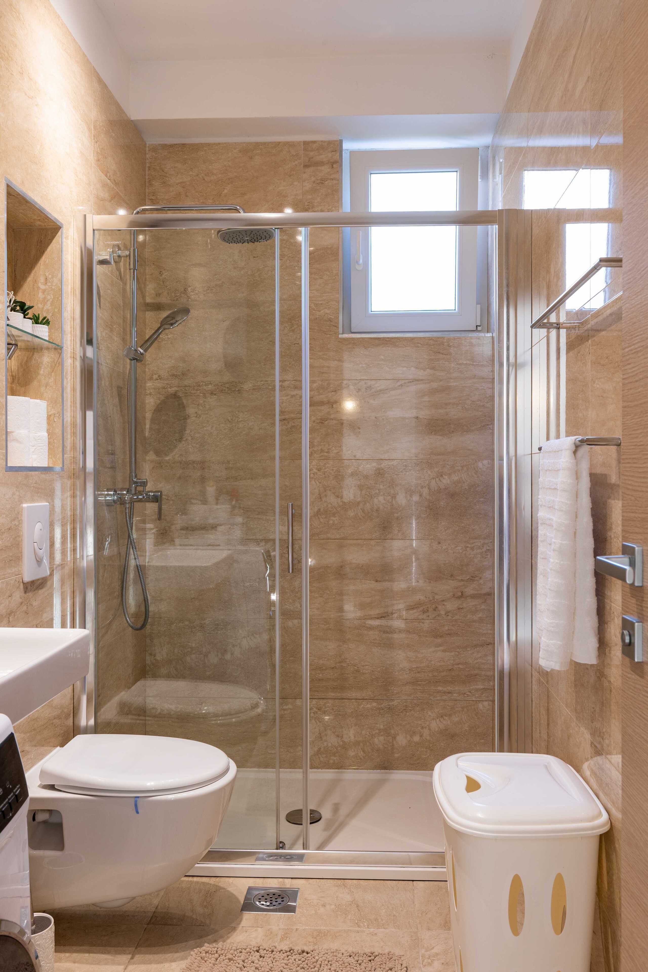A modern bathroom with a glass-enclosed shower, a toilet, and a trash bin.