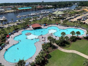 A large outdoor swimming pool with multiple lanes, surrounded by palm trees and a marina with boats.