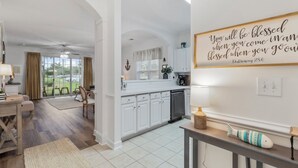 Une cuisine spacieuse avec des meubles blancs, un coin repas doté d’une table en bois et une vue sur l’extérieur grâce à de grandes fenêtres.