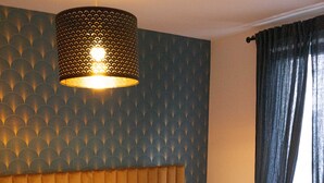 Una habitación de hotel con cama, cabecera, pared con diseño geométrico, lámpara colgante y ventana con cortinas.