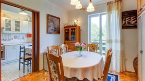A dining area with a round table, chairs, a chandelier, a cabinet, and a window with curtains. - Apartment Blamax (Mali Losinj)