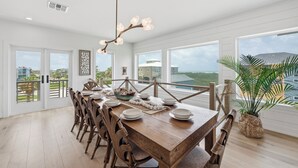A spacious dining area with a wooden table set for six, large windows offering a view of the landscape, and a ceiling light fixture.