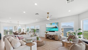 A spacious living room with a large TV, comfortable seating, a ceiling fan, and a view of the outdoors.