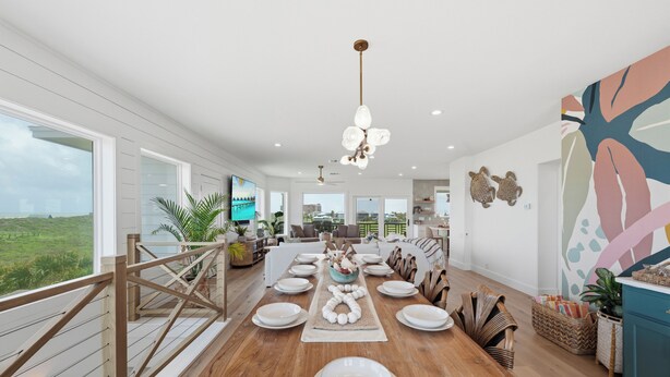 A spacious dining area with a wooden table set for a meal, a balcony with a railing, and a view of the landscape.