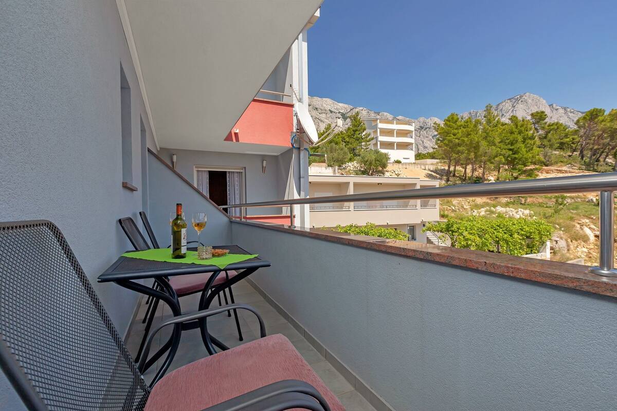 Een balkon met een tafel voor twee personen, een stoel en een fles wijn.