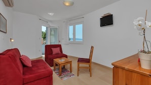 A living room with a red sofa, a wooden coffee table, a red armchair, and a wooden cabinet with a potted plant.