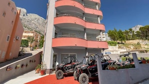 A multi-story building with balconies, a red carpet, and off-road vehicles parked in front.