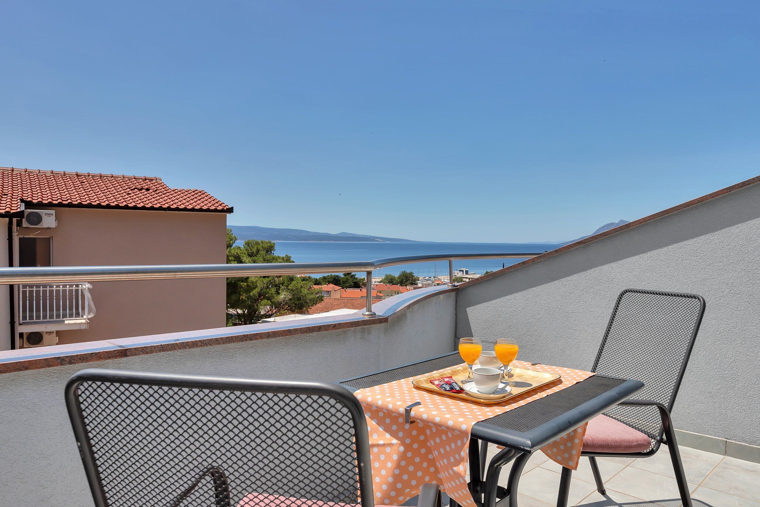 A balcony with a table set for breakfast, overlooking a scenic view of the sea and distant mountains.